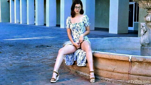 Ellie Nova in short floral dress, legs spread teasingly on fountain edge