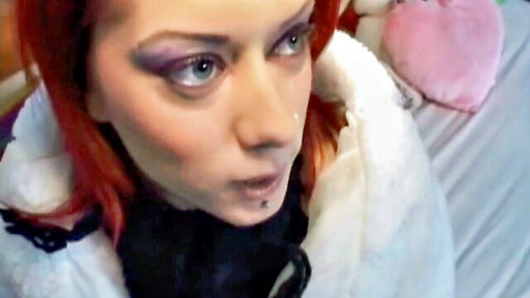 Seductive redhead goth woman with lip piercing and heavy makeup stares hungrily close-up on bed