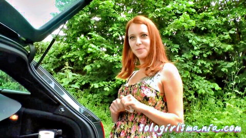 Redhead woman in floral dress standing by car trunk outdoors on road trip
