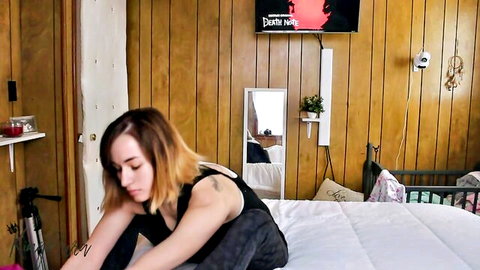 Naughty brunette in tank top sitting cross-legged on bed teasing in bedroom