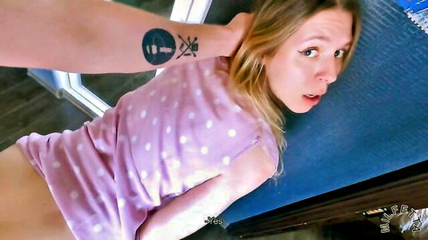 Tattooed hand grips blonde's neck firmly as she lies back surprised with wide eyes, open mouth and bare pussy exposed
