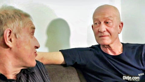 Two elderly men chatting casually on a couch in casual shirts