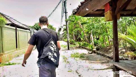Indonesian man walking down village alley in black t-shirt and pants with backpack