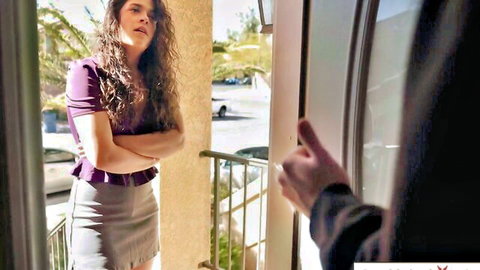Victoria Voxxx in purple blouse and gray mini skirt, arms crossed at door