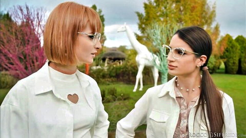 Dolly Dyson in glasses and white outfit chatting outdoors with brunette