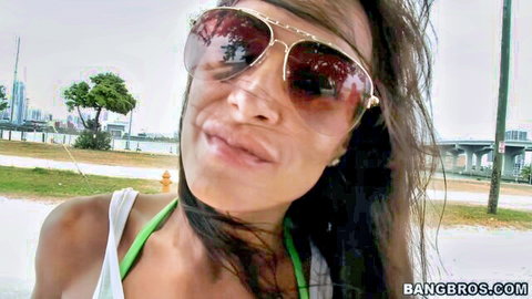 Tanned brunette MILF with huge tits pouting seductively in white tube top and sunglasses outdoors