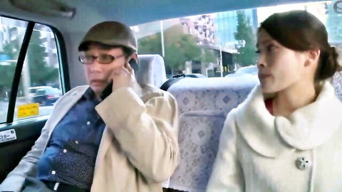 Japanese woman in white coat sits beside older man talking on phone in taxi cab
