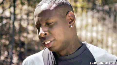 Intense close-up of Black man's face with earrings outdoors in gray hoodie