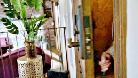 Hands gripping open bedroom door with plants and purple chair in cozy interior tease