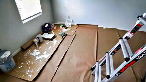 Empty bedroom renovation scene with ladder, paint cans, drop cloths, and tools on floor