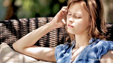 Blonde teen teases outdoors lounging on wicker chair with slipping blue top