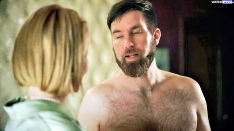 Blonde woman in satin top faces shirtless hairy-chested bearded man in intimate bedroom stare