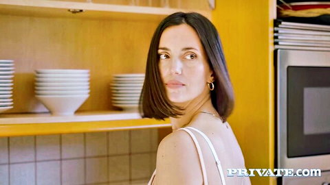 Sexy brunette in tight white tank top standing in yellow kitchen from behind
