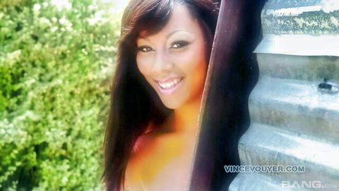 Sexy smiling Asian brunette with huge cleavage peeking from metal fence voyeur style
