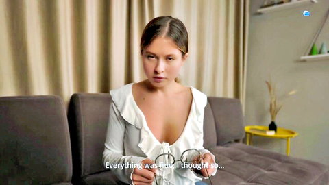Seductive MILF in low-cut white blouse showing deep cleavage on couch
