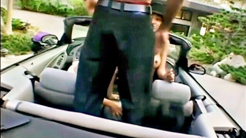 Man stands in outdoor convertible as two topless women grope his bulging cock and exposed tits
