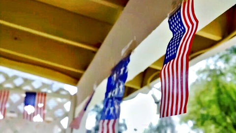 Patriotic American flags hanging from wooden porch ceiling with green leaves background