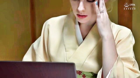 Young Japanese woman in traditional kimono thoughtfully using laptop at desk