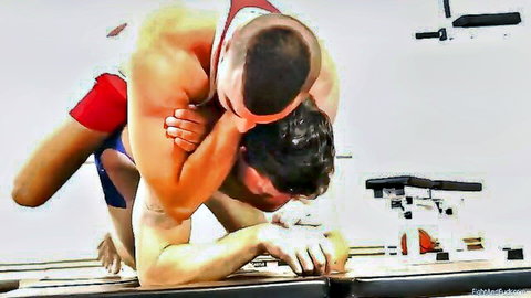 Muscular gay wrestlers in tight red singlets grappling dominantly on gym mat