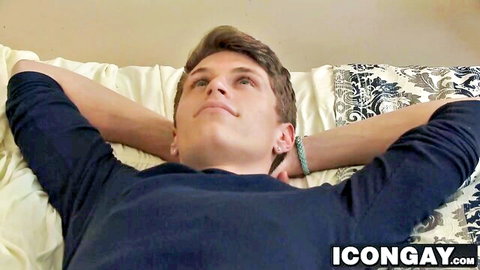 Young athletic gay guy with short hair lying on bed arms raised looking up seductively