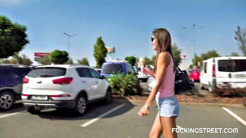 Brunette babe in pink tank top and tiny denim shorts struts in outdoor parking lot