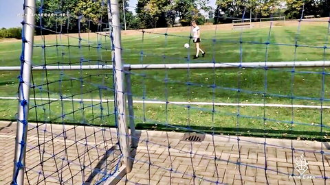 Skinny teen girl in white sports kit walks with soccer ball on outdoor field near goalpost