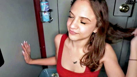 Callie Klein smiling in red tank top, cleavage visible in gloryhole setup