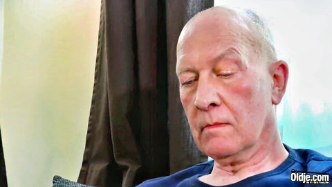 Close-up of bald older man with eyes closed and intense expression in blue shirt
