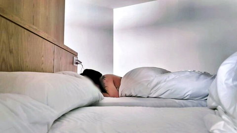 Asian woman with black hair sleeping nude under white sheets in bed