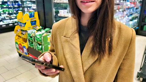 Smiling hot teen in coat holding phone in grocery store