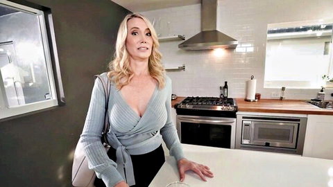 Blonde mature woman in low-cut blue wrap sweater showing deep cleavage