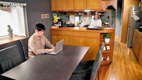 Japanese housewife in tight white top smiles at man using laptop in modern kitchen teasing foreplay