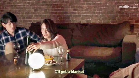 Young Asian woman in sweater pouring wine for boyfriend on cozy couch