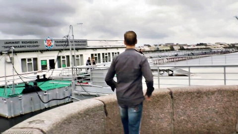 Man in gray shirt and jeans standing with back view at riverside dock by white boat
