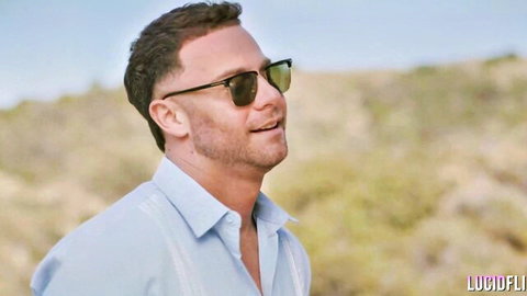 Handsome Caucasian man with stubble in sunglasses and light shirt, smiling outdoors