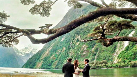 Outdoor wedding ceremony with bride in white dress and two grooms in suits amid mountains