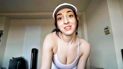 Hot brunette in low-cut tank top and visor smiles teasing her big tits cleavage