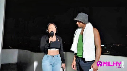 Thaina Fields in crop top and jeans with muscular man on outdoor stage