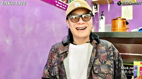 Smiling Asian man with long hair in Dodgers cap and sunglasses at festival counter, Enkai Thank You Festival EP2