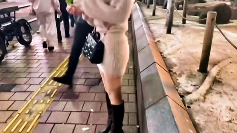 Slim Asian woman in short white knit dress and black boots walking outdoors at night