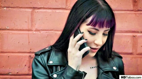 Seductive brunette with purple streaks in leather jacket talks on phone showing chest tattoos