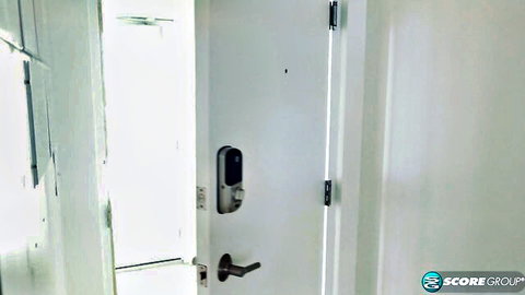 White door ajar with smart lock and handle in dimly lit room