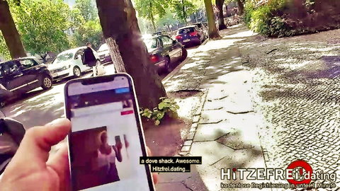 Hand holding smartphone displaying Hitzerfrei hot free dating app promo in sunny outdoor park