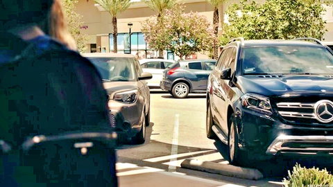 Blonde woman in black top walking in sunny parking lot near Mercedes SUV