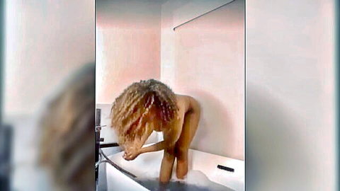Curly-haired ebony woman nude bending over bathtub edge