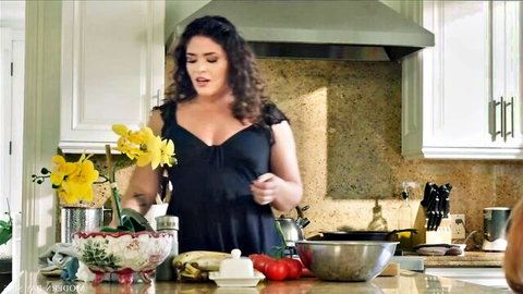 Curvy brunette in low-cut black dress prepares veggies in kitchen tease
