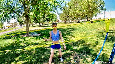 Muscular young trans babe in tiny yellow shorts and blue crop top posing with volleyball in public park