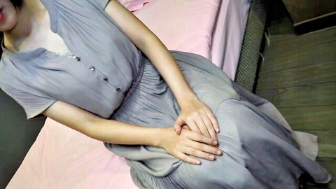 Slim Asian woman in light blue button dress sitting on bed