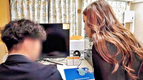 Long-haired brunette woman and curly-haired man intently viewing computer screen at desk