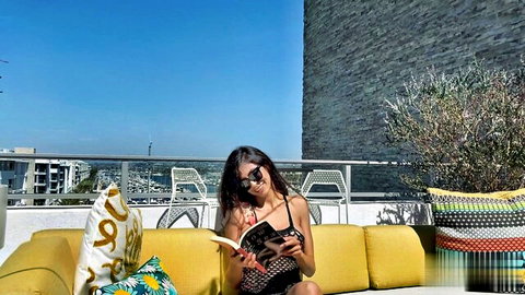 Tanned brunette MILF in black bikini with big tits reads book on sunny rooftop